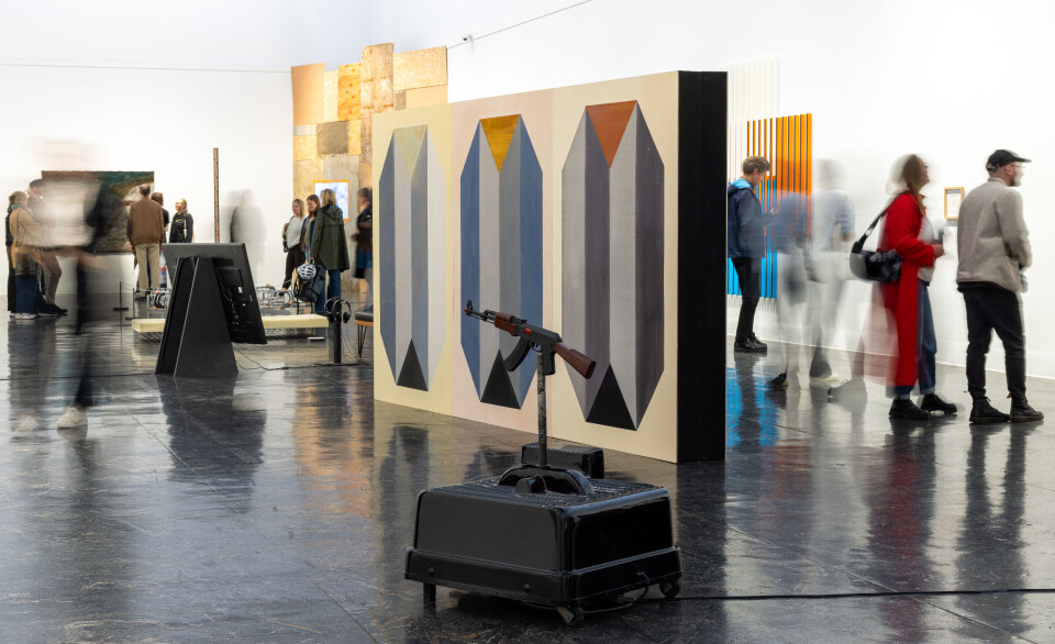 I forkant står installasjonen «NO MORE WAR / Geværenes bønn» (2025) av Elin Austbø. I bakgrunnen ser me måleria «Kapsel» og «Sol» av Endre Opheim.