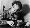 WOODY GUTHRIE (1912-1967). American folk singer. Photographed playing a guitar that has a sticker attached reading: 'This Machine Kills Fascists.' Photograph by Al Aumuller, 8 March 1943.