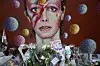 Caption: FILE - In this Tuesday, Jan. 12, 2016 file photo, tributes lie beneath a mural of singer David Bowie by artist Jimmy C in Brixton, south London. Bowie, the other-worldly musician who broke pop and rock boundaries with his creative musicianship, nonconformity, striking visuals and a genre-spanning persona he christened Ziggy Stardust, died of cancer Sunday aged 69. He was born in Brixton. (AP Photo/Matt Dunham)